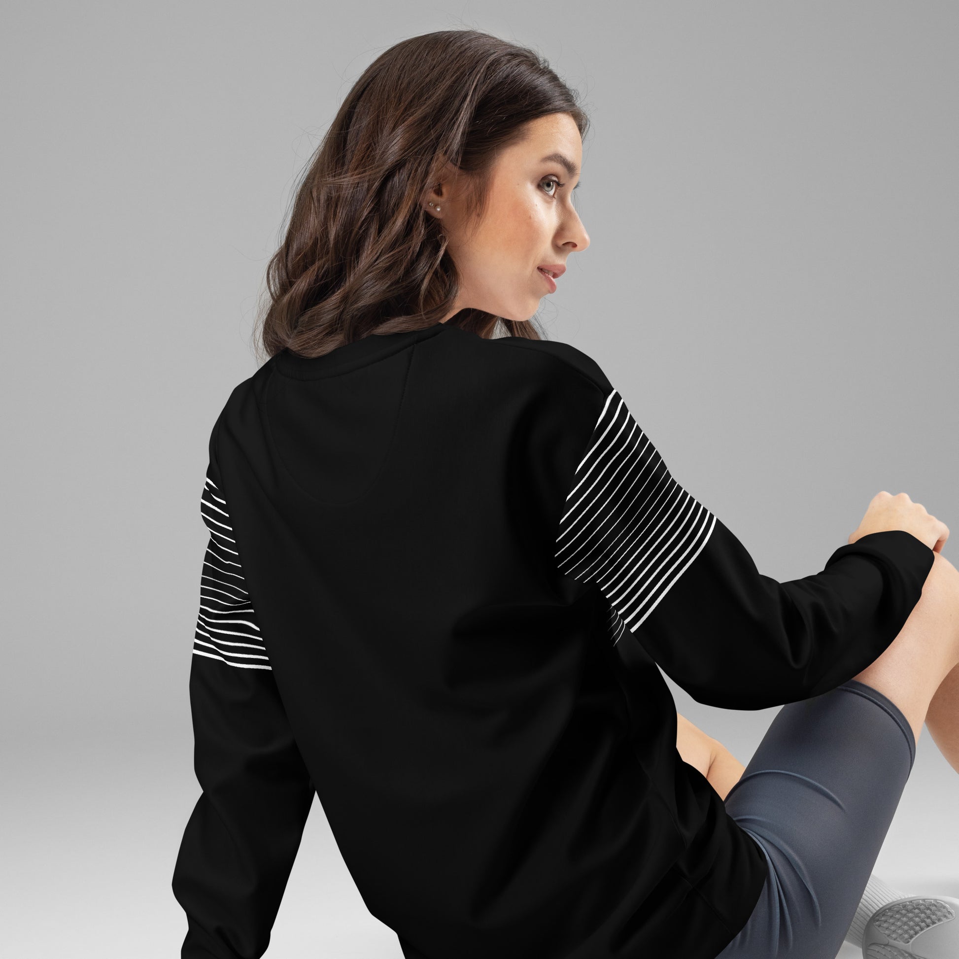 Back view of woman wearing black unisex sweatshirt with white striped sleeve details and plain black back